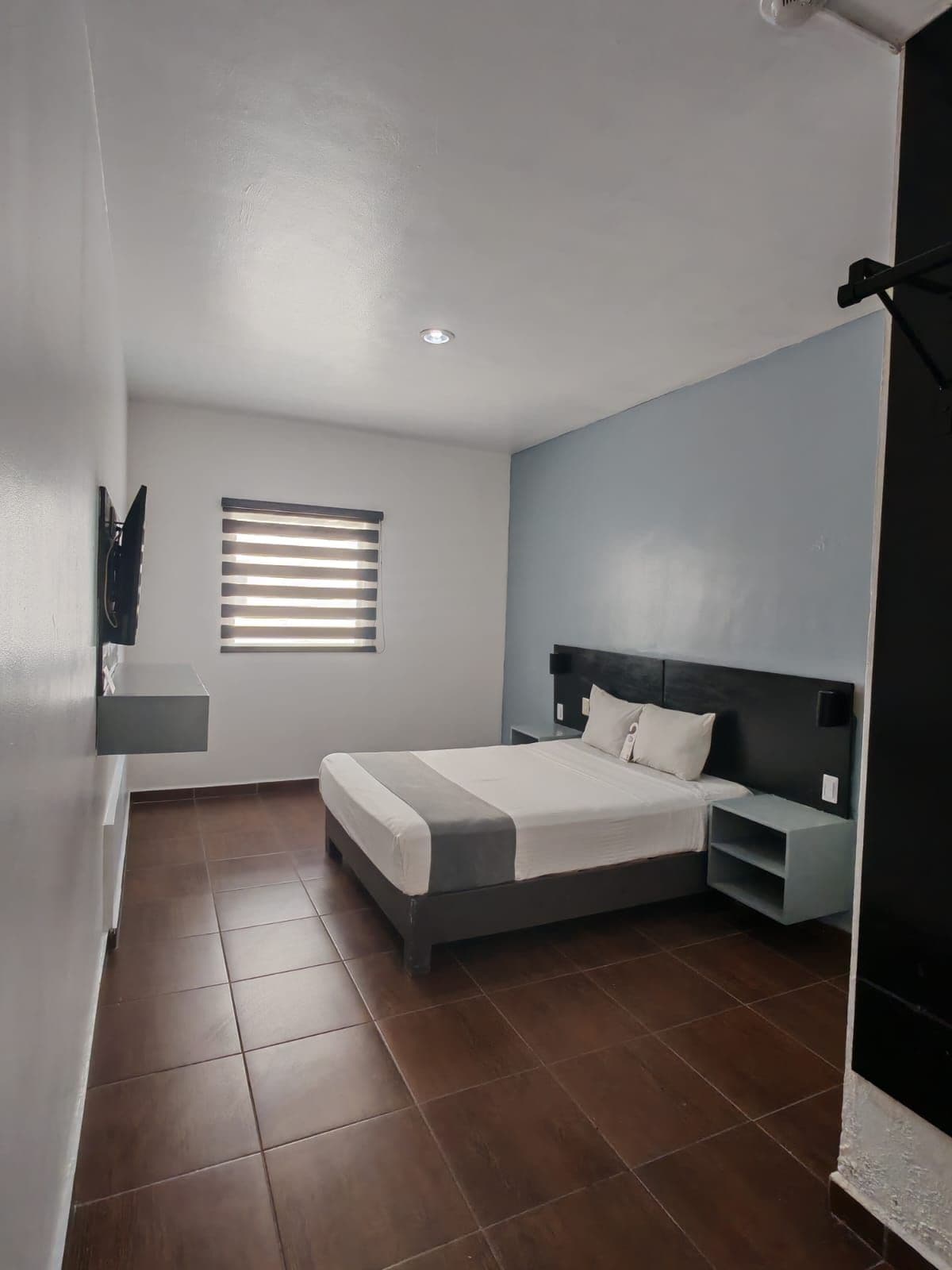 Un dormitorio moderno con cama, mesitas de noche, ventana con persianas y estante en la pared.