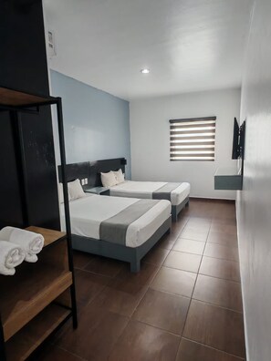 A hotel room with two beds, a TV, a window with blinds, and a shelf with towels. - Alo Select Mazatlan (Mazatlán)