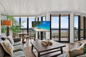 A spacious living room with a large TV, comfortable seating, and a view of the ocean.