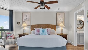 Ein Schlafzimmer mit einem großen Bett, zwei Nachttischlampen, einem Deckenventilator und Kunstwerken an den Wänden.