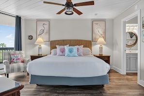 A bedroom with a large bed, two bedside lamps, a ceiling fan, and artwork on the walls.