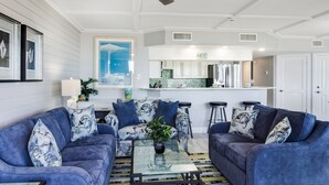 A living room with two blue sofas, a glass coffee table, and a ceiling fan.