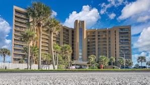 A multi-story hotel with balconies, palm trees, and a clear blue sky.