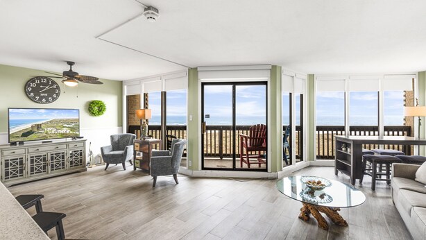 A spacious living room with a balcony, a large clock, and a television.