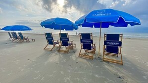 Beach chairs and umbrellas with "SANDPIPER CONDOMINIUMS" branding on a sandy beach.