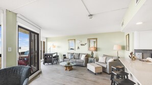 A spacious living room with a large window, a sofa, a coffee table, and a kitchen area with a counter and stools.