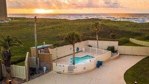 A pool area with a view of the ocean, surrounded by a fence and palm trees.