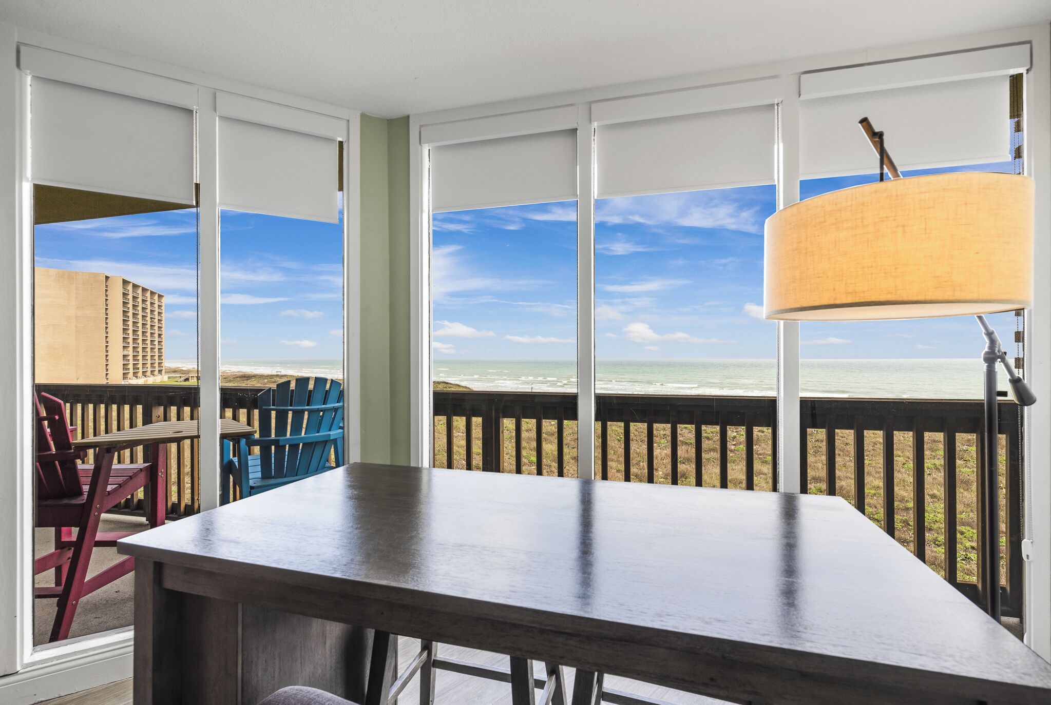 Ein Zimmer mit großem Fenster mit Blick auf einen Strand, einem Holztisch und zwei Stühlen.