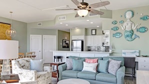 A modern living room with a teal sofa, a round coffee table, and a ceiling fan. - Sandpiper Condominiums 1208, Panoramic Gulf Views w/ direct access to Mustang Island/Port A beaches. (Port Aransas)