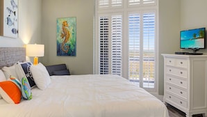 A bedroom with a bed, pillows, a dresser, a television, and artwork on the walls. - Sandpiper Condominiums 1208, Panoramic Gulf Views w/ direct access to Mustang Island/Port A beaches. (Port Aransas)