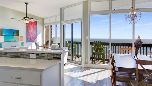 A spacious kitchen with a large island, a dining area with a view of the ocean, and a balcony with outdoor seating. - Sandpiper Condominiums 1208, Panoramic Gulf Views w/ direct access to Mustang Island/Port A beaches. (Port Aransas)