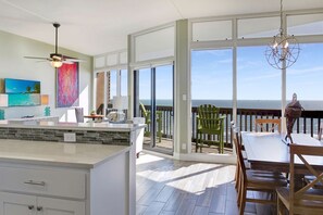Une cuisine spacieuse avec un grand îlot central, un coin repas offrant une vue sur l’océan et un balcon avec un espace salon extérieur.