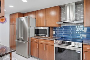 A modern kitchen with stainless steel appliances, wooden cabinets, and blue-tiled backsplash.
