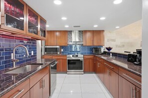 Una cocina moderna con electrodomésticos de acero inoxidable, armarios de madera y salpicadero de azulejos azules.