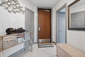 A hallway with a wooden door, a metal-framed mirror, and a glass cabinet with decorative items.