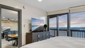 Ein Hotelzimmer mit einem großen Bett, einem Fernseher auf einem Schrank, einem Balkon mit Meerblick und einem Essbereich mit Tisch und Stühlen.