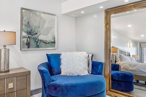 Un dormitorio moderno con un sillón azul, un cuadro abstracto grande, un espejo y un armario de madera.