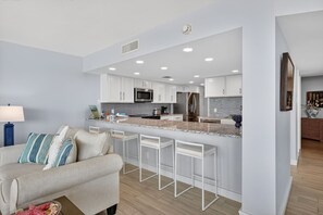 Une cuisine moderne avec des meubles blancs, un îlot central doté de tabourets, un four à micro-ondes et un réfrigérateur.