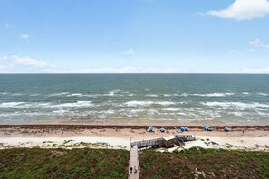Une plage avec une promenade en bois menant à une construction, une rive sablonneuse et l’océan.