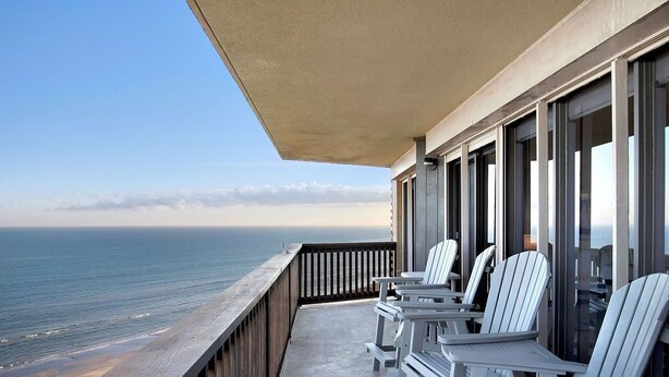 A balcony with white Adirondack chairs and a view of the ocean.
