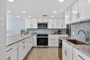 Une cuisine moderne avec des meubles blancs, un four en acier inoxydable, un four à micro-ondes et un plan de travail en granit.