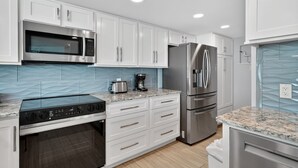 A modern kitchen with white cabinets, stainless steel appliances, a built-in oven, and a granite countertop.