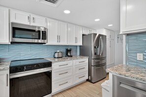 A modern kitchen with white cabinets, stainless steel appliances, a built-in oven, and a granite countertop.