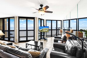 A spacious balcony with a television, seating area, and a ceiling fan.