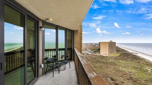 Un balcón con puertas de vidrio, suelo de concreto y vista a la playa y al océano.