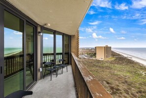 A balcony with glass doors, a concrete floor, and a view of the beach and ocean.