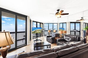 A spacious living area with a balcony, leather sofas, a coffee table, and a television.