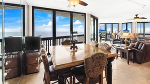A spacious living area with a large wooden table, comfortable seating, and a balcony with a view of the ocean. - Sandpiper Condominiums 1104, Panoramic Gulf Views w/ direct access to Mustang Island/Port A beaches. (Port Aransas)