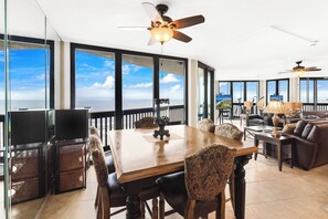 Un vaste espace de vie comprenant une grande table en bois, des sièges confortables et un balcon offrant une vue sur l’océan.