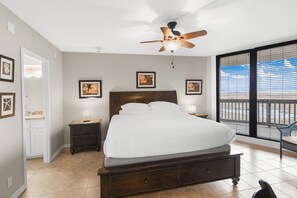 A bedroom with a bed, a nightstand, a ceiling fan, and a window with a view.