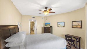 A bedroom with a bed, a desk, a chair, a ceiling fan, and a door leading to a bathroom. - Sandpiper Condominiums 1104, Panoramic Gulf Views w/ direct access to Mustang Island/Port A beaches. (Port Aransas)