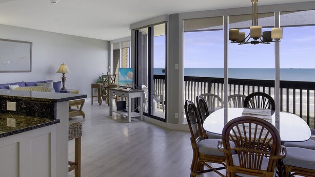 Un vaste espace de vie avec un balcon donnant sur la mer, une table à manger avec des chaises et un coin cuisine.