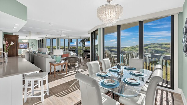 A spacious living area with a large dining table set for six, a chandelier, and a view of the landscape through large windows.