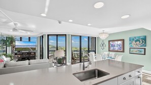 A modern kitchen with a large island, a dining area with a view, and a living room with a large window overlooking a scenic landscape.
