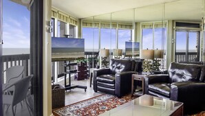 A spacious living room with a large window overlooking a balcony, leather sofas, a coffee table, and a view of the ocean. - Sandpiper Condominiums 1104L, Panoramic Gulf View w/ direct access to Mustang Island/Port A beaches. (Port Aransas)