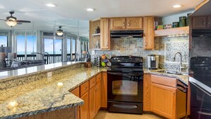 A modern kitchen with granite countertops, wooden cabinets, a built-in oven, and a large island with seating. - Sandpiper Condominiums 1104L, Panoramic Gulf View w/ direct access to Mustang Island/Port A beaches. (Port Aransas)