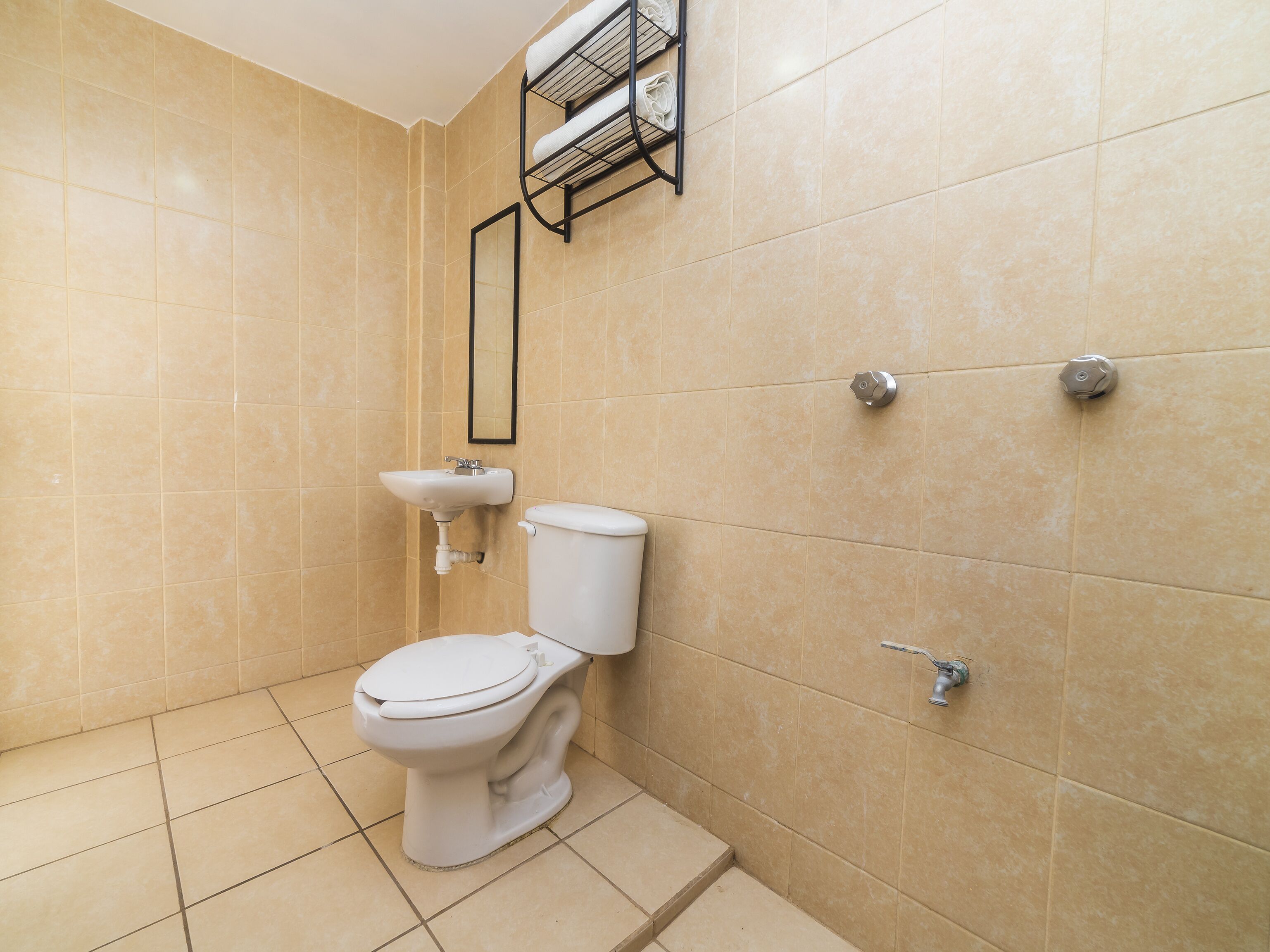 Une salle de bain avec des carreaux de couleur beige, des toilettes blanches, un lavabo et un porte-serviettes.