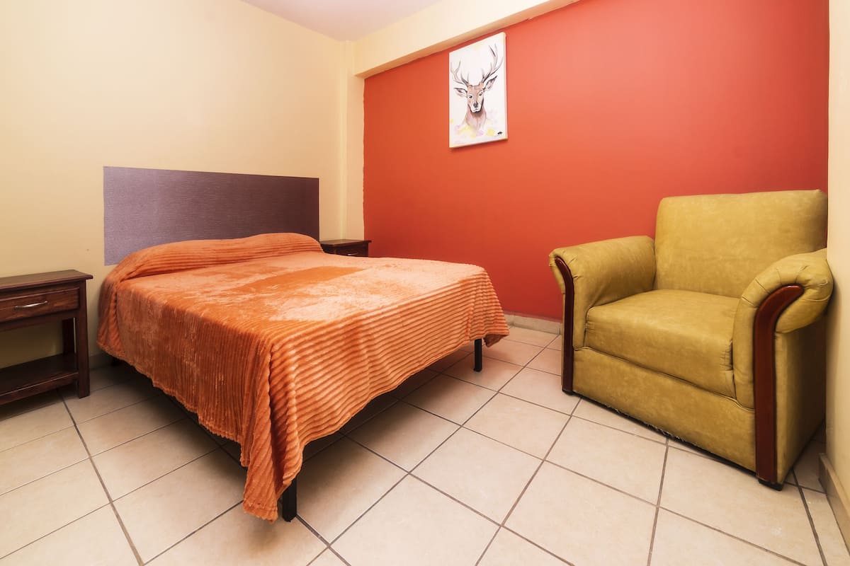 Un dormitorio con una cama, una silla, una mesita de noche y un cuadro en la pared.