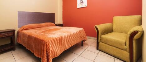 Un dormitorio con una cama, una silla, una mesita de noche y un cuadro en la pared.