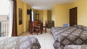 Habitación de hotel con dos camas, una mesa de comedor, sillas, un televisor y una ventana con cortinas.