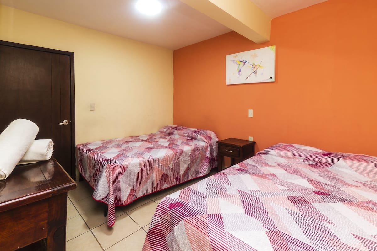 Una habitación con dos camas, una mesita de noche de madera, una puerta y un cuadro colgado en la pared.