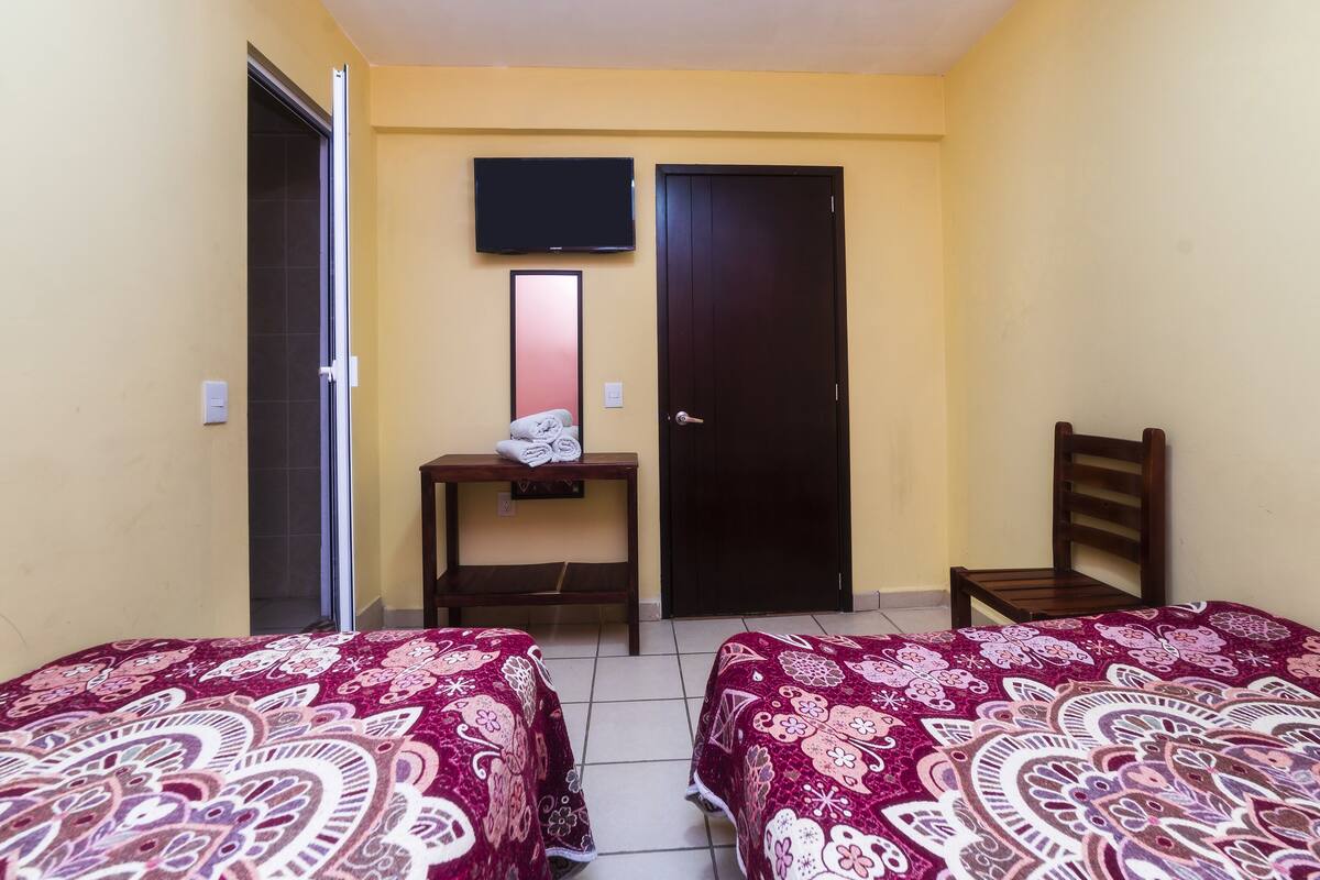 Habitación de hotel con dos camas, un televisor sobre una puerta, una mesita con toallas y una silla.