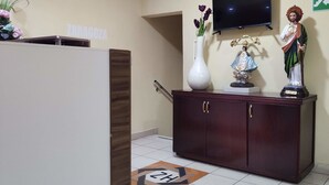 Zona de recepción con un mueble de madera, un televisor montado en la pared y una estatua encima.