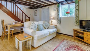 Un salon chaleureux avec un escalier en bois, un canapé, une table basse, un meuble pour la télévision et une fenêtre avec des rideaux.