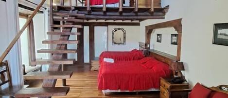 Un interior rústico con una escalera de madera que sube a un dormitorio en el altillo, un sofá rojo y una mesa de centro de madera.