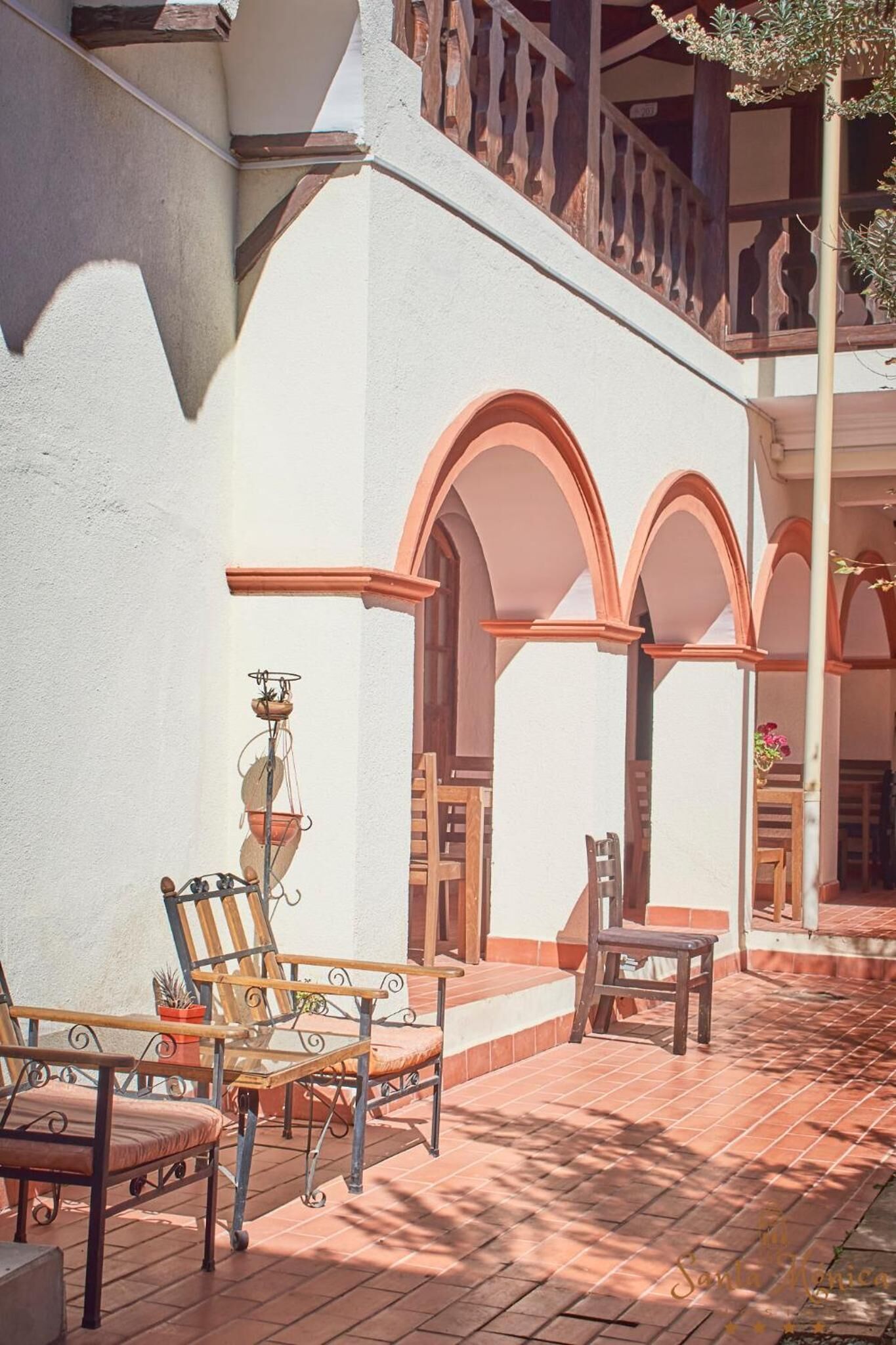 A courtyard with a white building, wooden furniture, and arches.